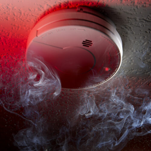 Close up shot of ceiling mounted smoke detector with white smoke and red warning light